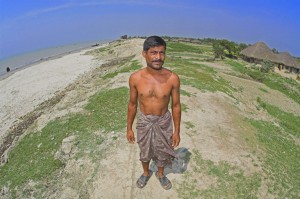 Colour photograph showing Ruhul Khan, who has lost three houses in recent years. His former homes were located to the left of the picture, an area now covered by water.