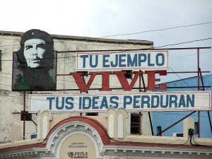 Colour photograph showing a hoarding on the roof of a building in Cienfuegos, Cuba ... which comprises an image of CHE, with the accompanying text "Tu Ejemplo Vive - Tus Ideas Perduran". Photograph by CJ Walsh. 2007-04-13. Click to enlarge.